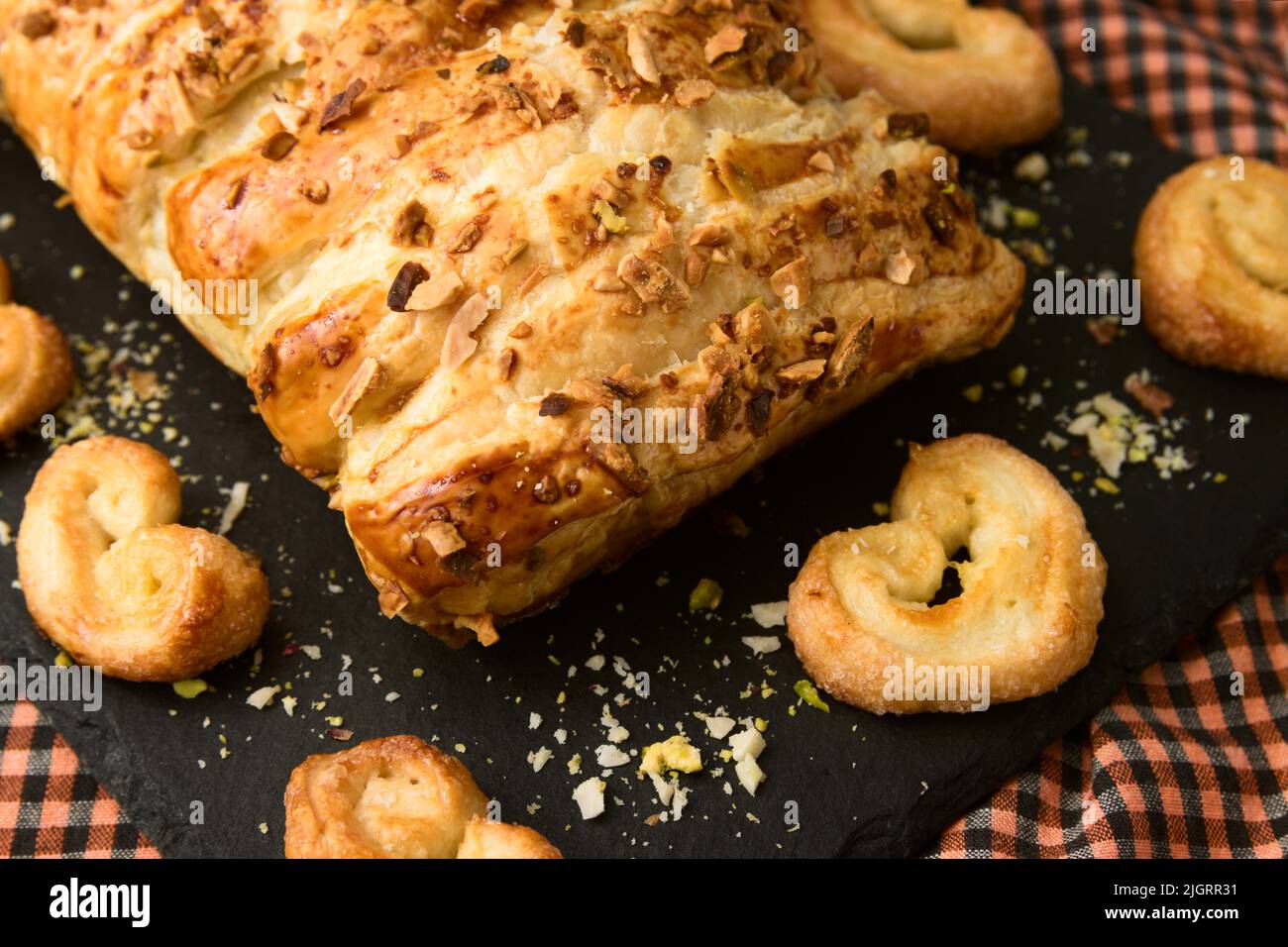Image of a puff pastry filled with chocolate or cocoa cream next to artisan puff pastry palm trees, all on a black slate plate Stock Photo