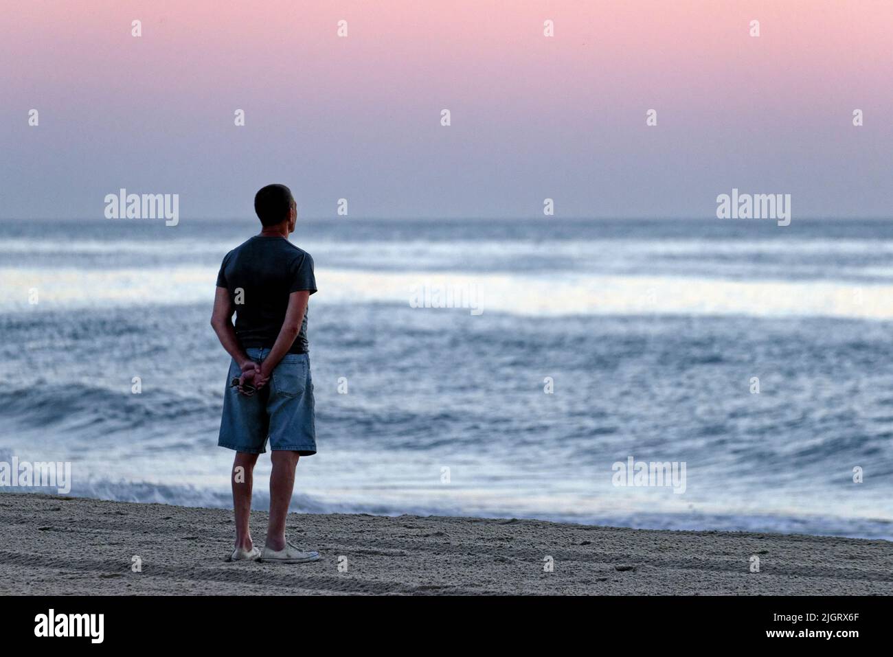 A solitary male figure contemplates a sunrise from the beach at Rehoboth Beach, Delaware USA. Stock Photo