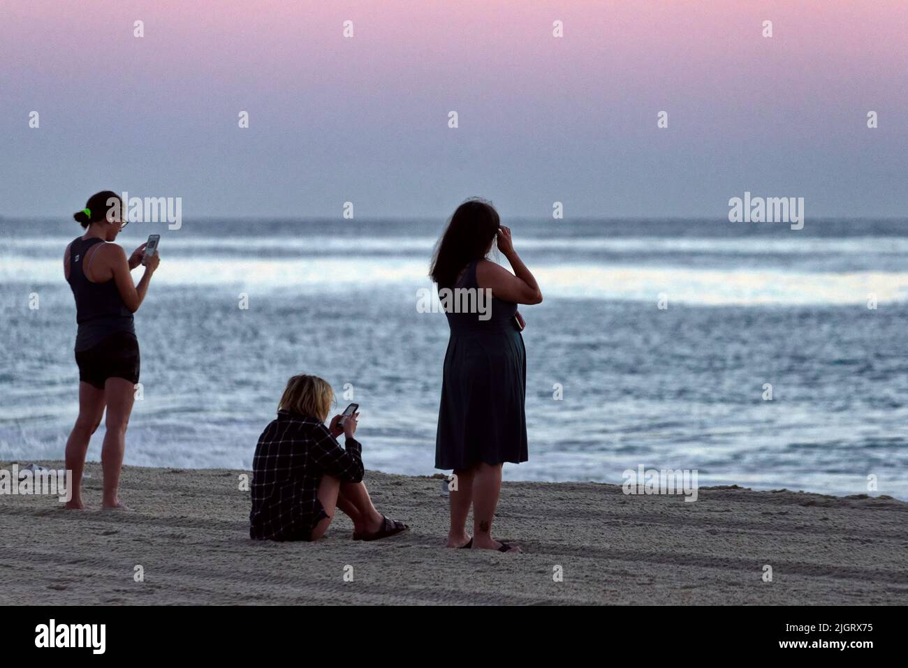 Three women observe a sunrise from the beach at Rehoboth Beach, Delaware USA. Stock Photo