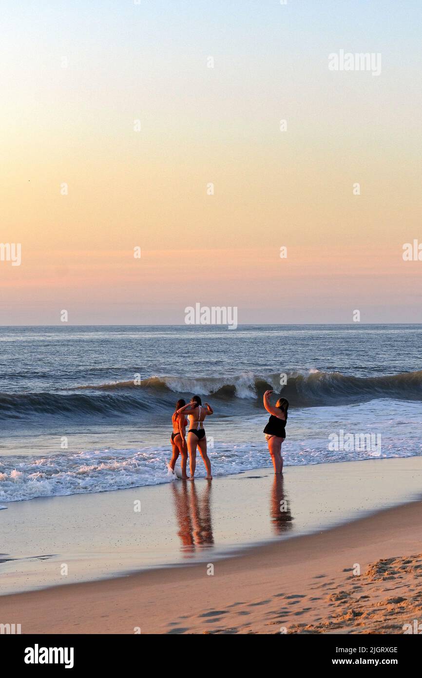 Three young women stand in the surf at Rehoboth Beach, Delaware USA during sunrise. Stock Photo