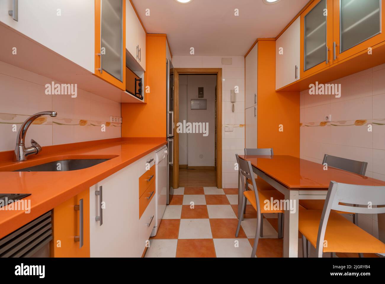 Kitchen with bright orange and white cabinets, orange stone countertop, gray accents, and the same tile floor and matching table. Stock Photo