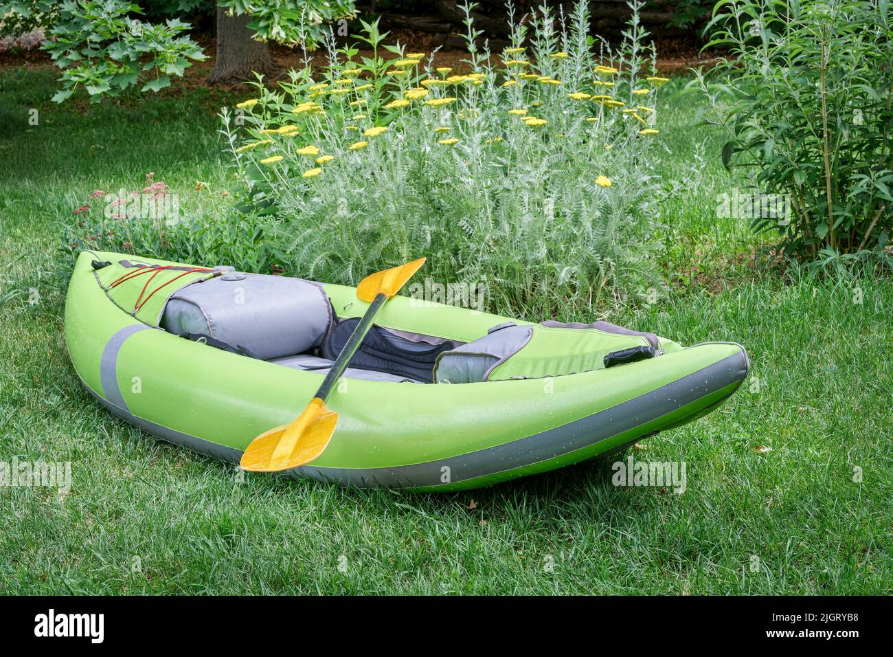 green inflatable whitewater one person kayak with a paddle in a backyard ready for a paddling adventure Stock Photo