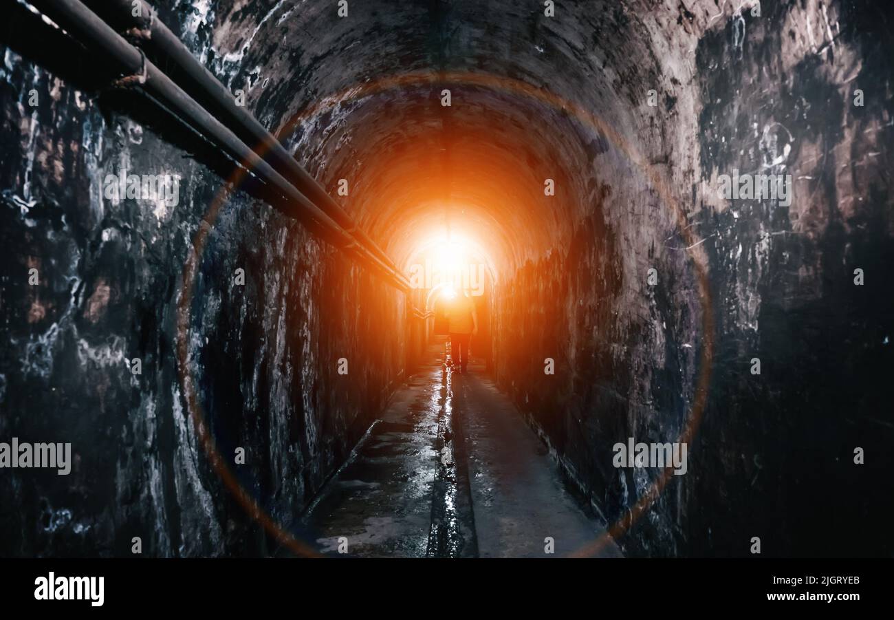 Light at end of underground tunnel. Silhouette of figure of man goes into light. Stock Photo
