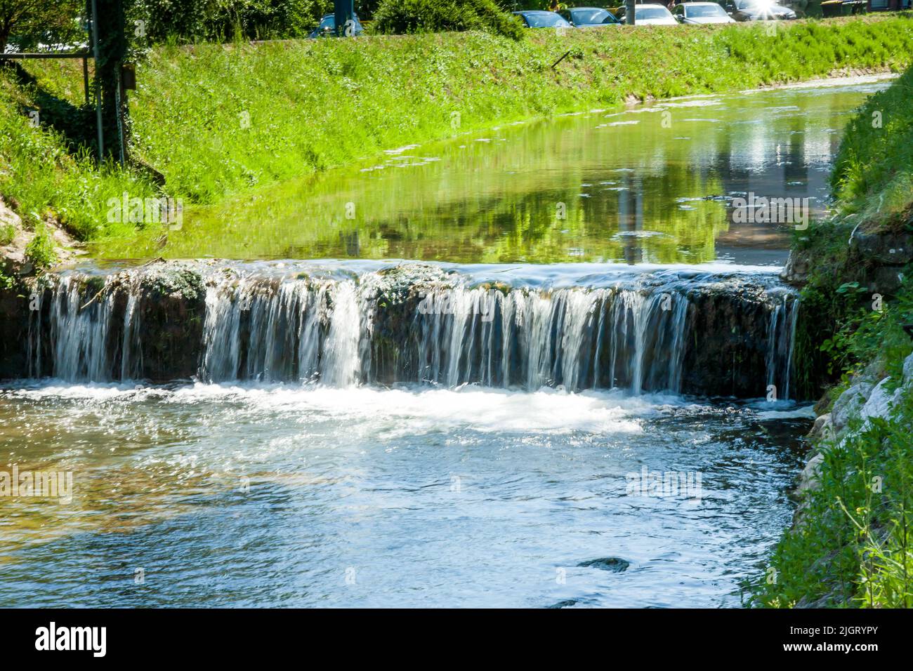 Beautiful small waterfall, cascading river against green vegetation Stock Photo