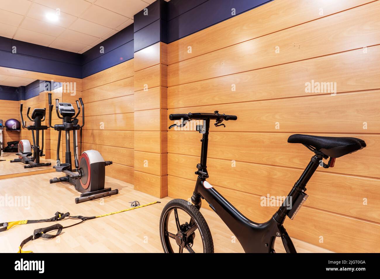 A gym room with exercise bikes, stairs and objects to perform various exercises and a large mirror that covers one of the walls and the other with che Stock Photo