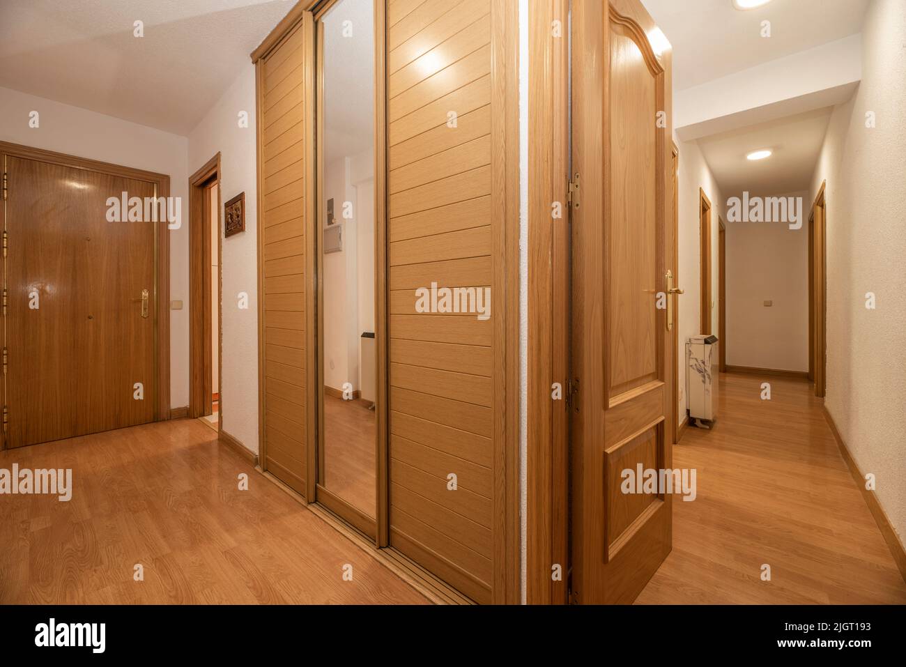 Hallways of a residential home with fitted wardrobes with sliding wooden doors and mirrors, matching oak wood flooring Stock Photo