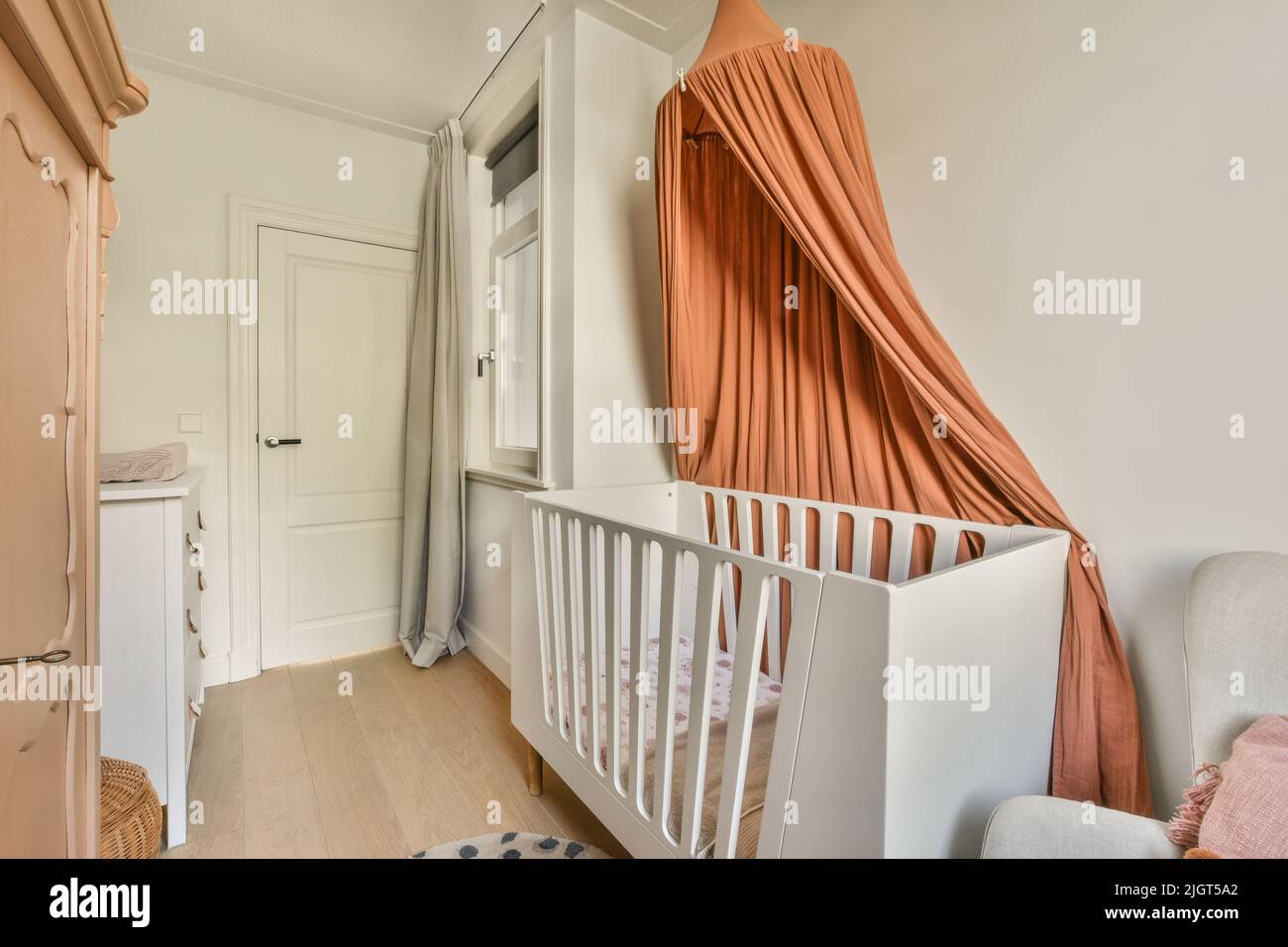 Interior of white room with baby crib and armchair near window with