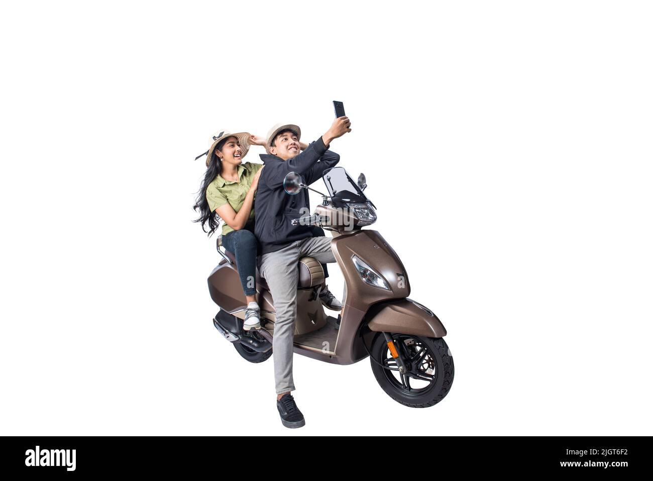 An Asian couple with a hat is sitting on a scooter and taking a self-portrait with a mobile phone isolated over white background Stock Photo