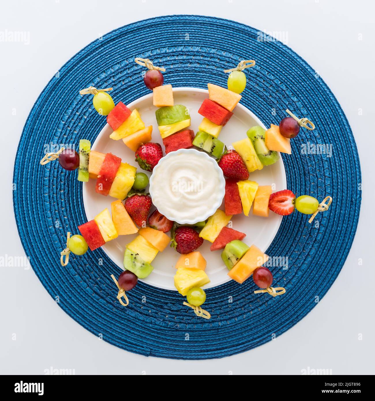 A round platter with fresh fruit skewers and yogurt dip in the middle