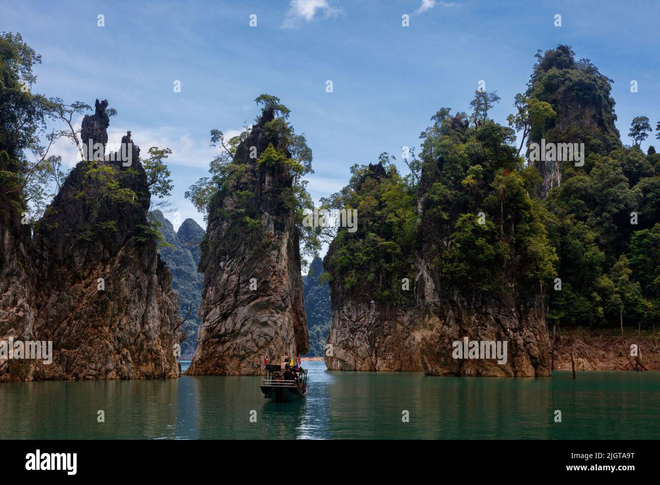 A long boat on Cheow lan lake in Khao Sok National Park isurrounded by tropical rain forest and karst formations - KHAO SOK, THAILAND Stock Photo