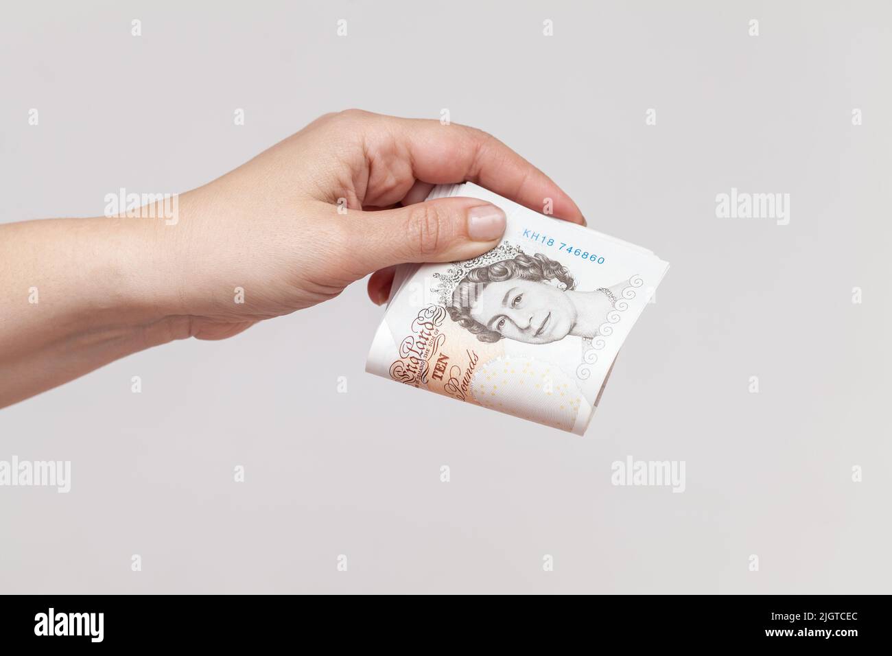 Stack of ten pound notes of the Bank of England in female hand. Close-up photo over gray wall background Stock Photo