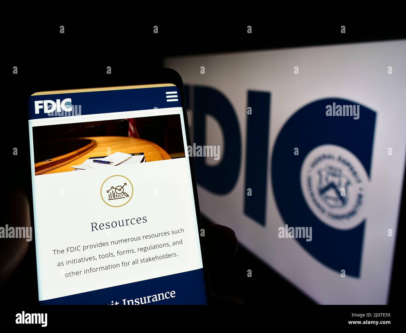 Person holding cellphone with webpage of US Federal Deposit Insurance Corporation (FDIC) on screen with logo. Focus on center of phone display. Stock Photo