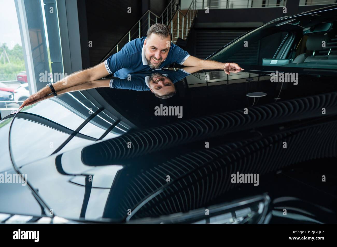 Happy caucasian man hugging the hood of his new car in a car dealership ...
