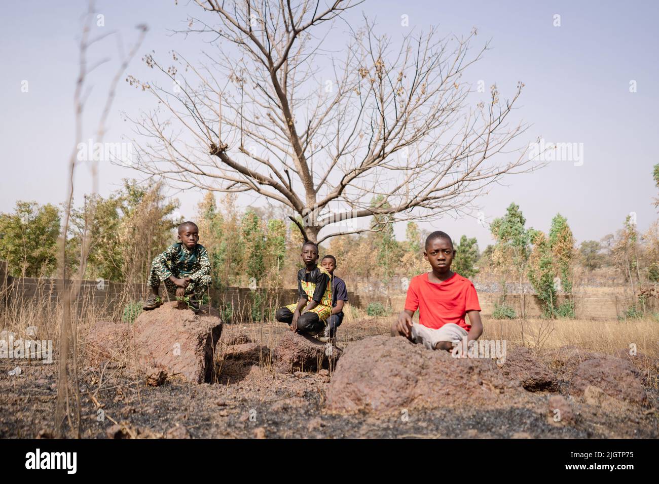 Group of four sad looking African boys sitting on a dried up farm doing nothing; crop failures, job losses, rising food prices, food speculation and p Stock Photo