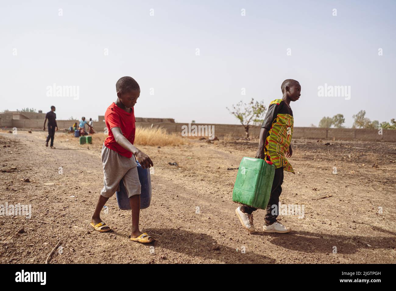 African children fetching water from a village pump; lack of houshold taps and child labour in developing countries Stock Photo