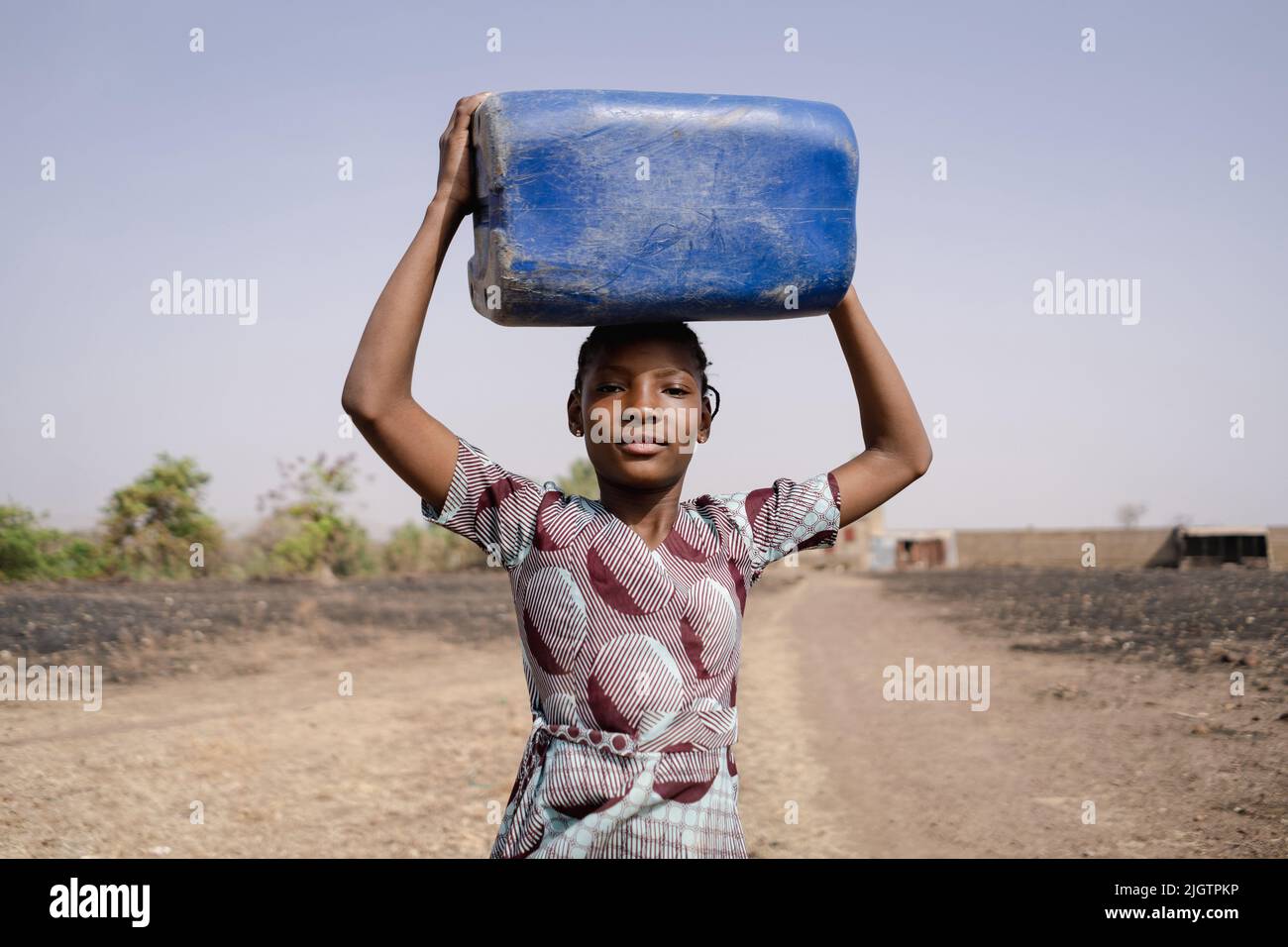 Young African girl carrying a heavy water container on her head, symbolising traditional roles of women in society blocking access to education, equal Stock Photo