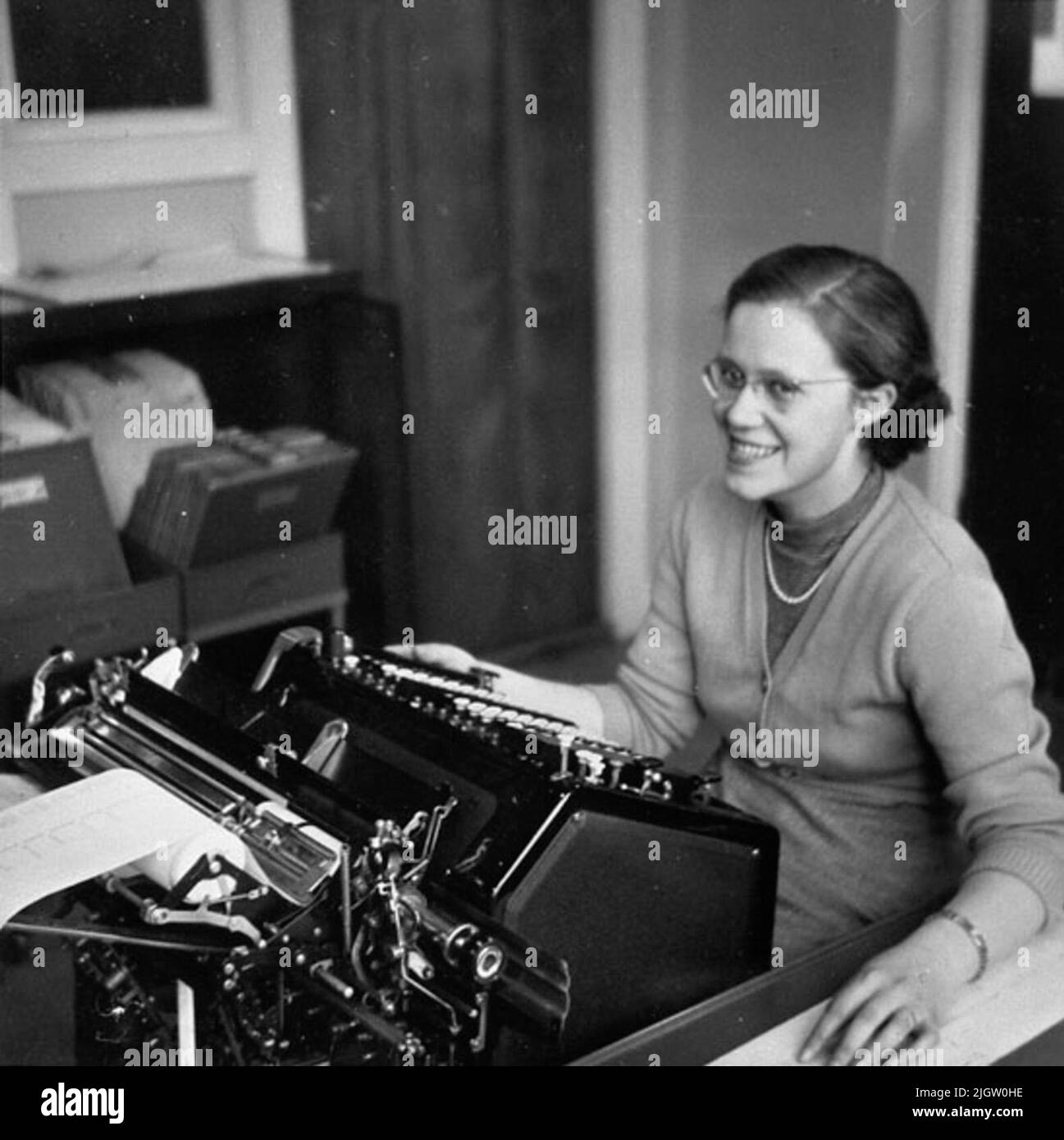 Photographer has also been Sven Åkerlund, Stockholm. It is unclear who is a photographer for each image. Sven Åkerlund died in the late 1900s. Bruno Elfving, Bohuslän Museum, has repro -photographed all pictures. Birgit holds one hand on the typewriter while the other rests on one disc. She looks happy and laughs at the photographer. Birgit wears the jumper set and pearl necklace as well as glasses. The curly hair has a side legs and is rejected behind the ears. Against the wall stands a open box that shows stored by mappar.se also UMFA53915: 0006 :: Stock Photo