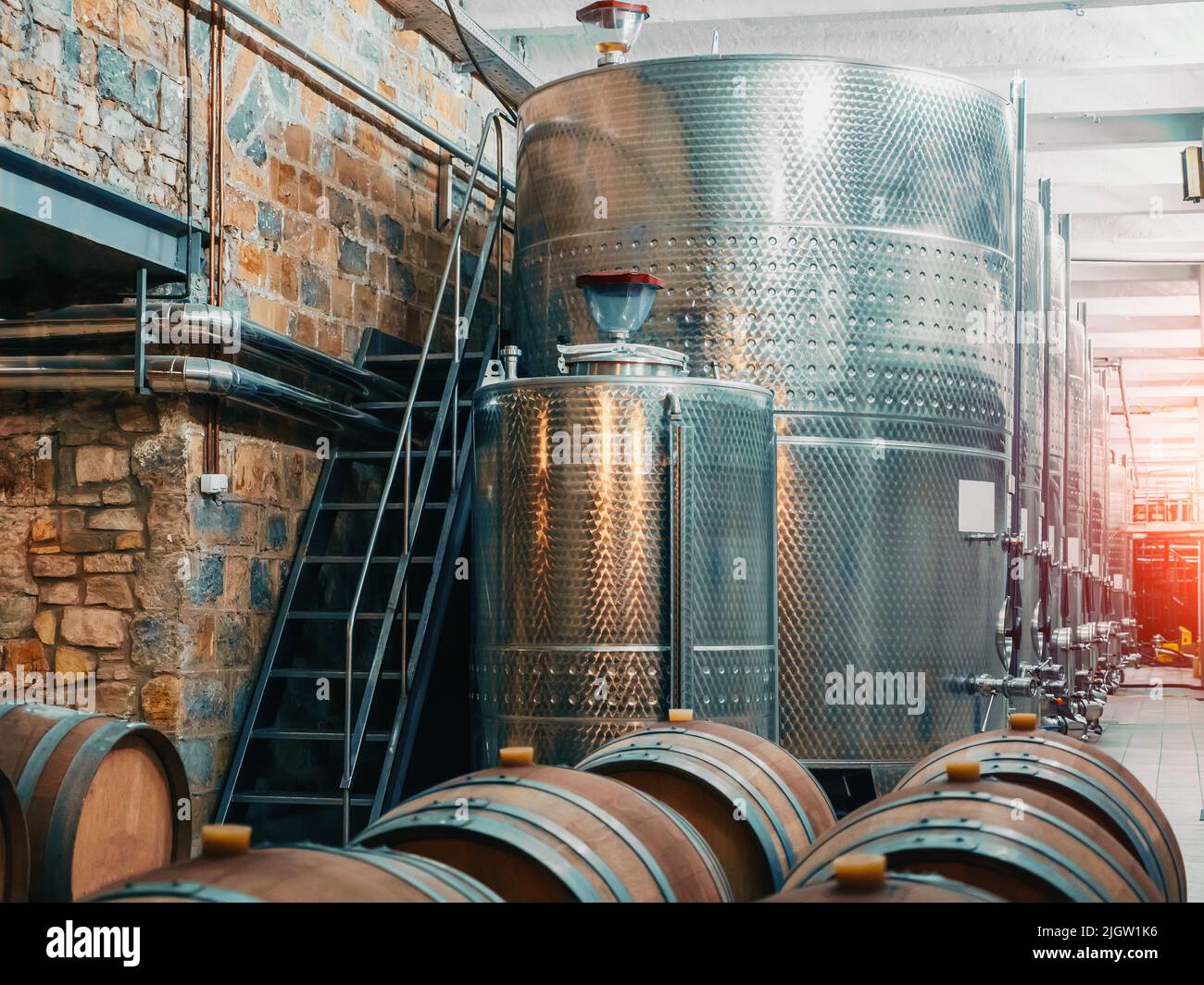 Winery factory with steel tanks for fermenting and wooden barrels for aging process, winemaking concept, food industry. Stock Photo