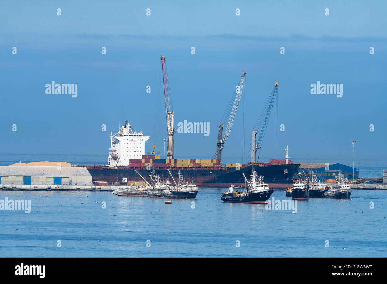 The port of Arica, Chile with commercial fishing boats and cranes loading containers on a cargo ship. Stock Photo