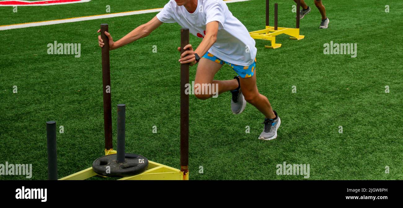 Runners pushing sleds with weights on a turf field during strength and agility drills at a high