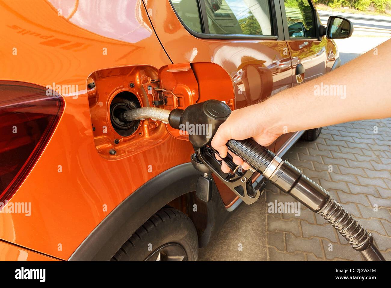 Petrol station pump. Pumping gasoline fuel in orange car at a gas station. Fill orange car with fuel in petrol station. Sunlight. Stock Photo
