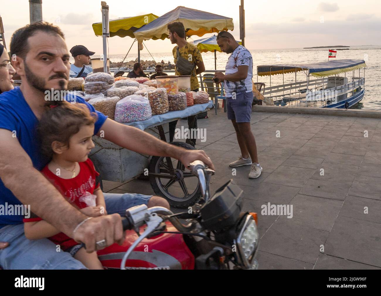 Man with his daughter riding his motorcycle along the sea, North Governorate, Tripoli, Lebanon Stock Photo