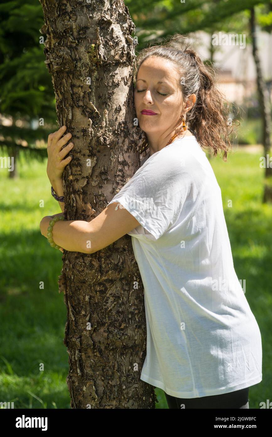 A woman sunbathes standing and hugging a tree. Hugging a tree has many