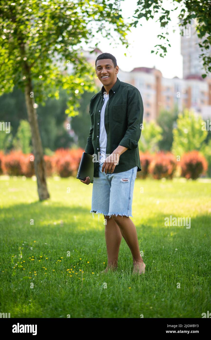 Man with laptop standing barefoot on grass Stock Photo