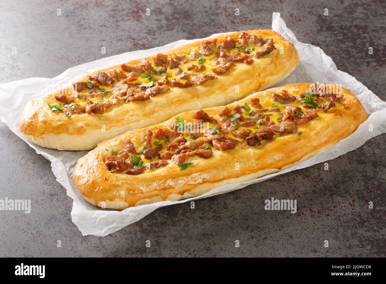 Pastrmajlija is an oval shaped pizza dough dressed with meat in the center and topped with an egg wash closeup on the parchment on the table. Horizont Stock Photo