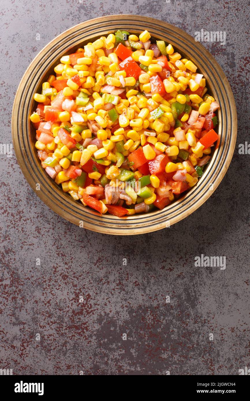 Corn chaat is an Indian snack made using sweetcorn kernels, onions, tomatoes, and a few herbs and spices on a plate closeup on the table. Vertical top Stock Photo