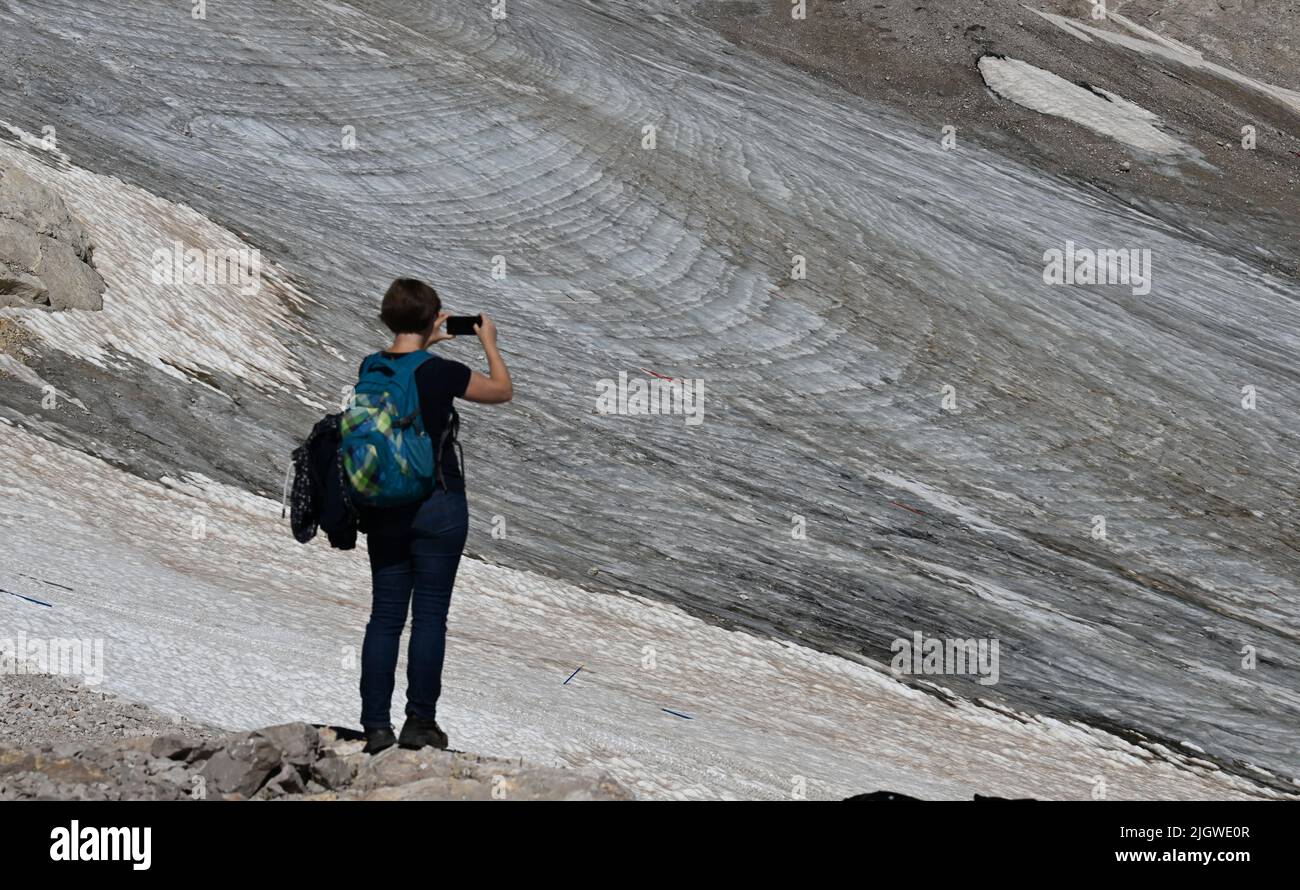Grainau, Germany. 13th July, 2022. A hiker photographs the remnants of the Northern Schneeferner Glacier on the Zugspitzplatt. The warm temperatures affected the remnants of the glacier on Zugspitze this summer. Credit: Angelika Warmuth/dpa/Alamy Live News Stock Photo