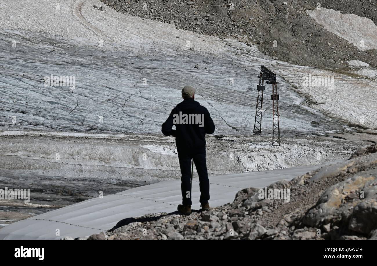 Grainau, Germany. 13th July, 2022. A hiker looks at the remains of the Northern Schneeferner Glacier on the Zugspitzplatt. The warm temperatures affected the remnants of the glacier on Zugspitze this summer. Credit: Angelika Warmuth/dpa/Alamy Live News Stock Photo