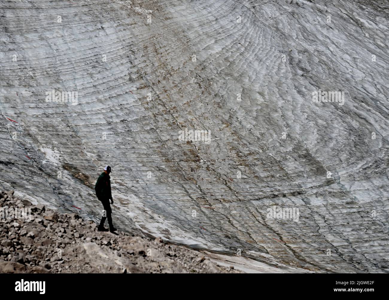 Grainau, Germany. 13th July, 2022. A vacationer stands on the Zugspitzplatt in front of the Northern Schneeferner Glacier. The warm temperatures affected the glacier remnant on the Zugspitze this summer. Credit: Angelika Warmuth/dpa/Alamy Live News Stock Photo