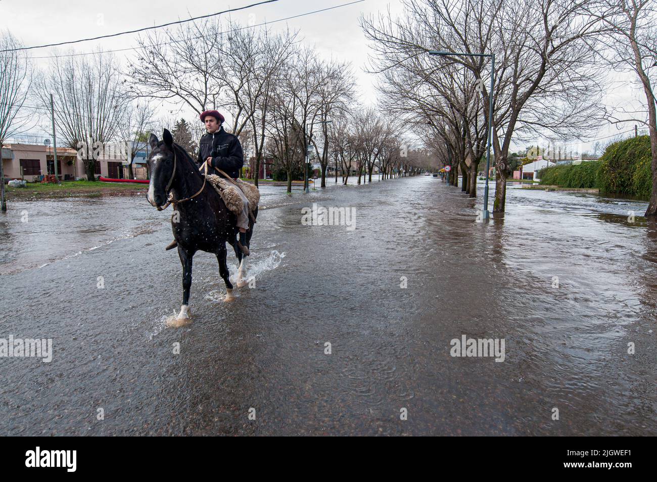 A Hispanic man riding a horse on the street because of floods in San Antonio de Areco, Buenos Aires, Argentina Stock Photo