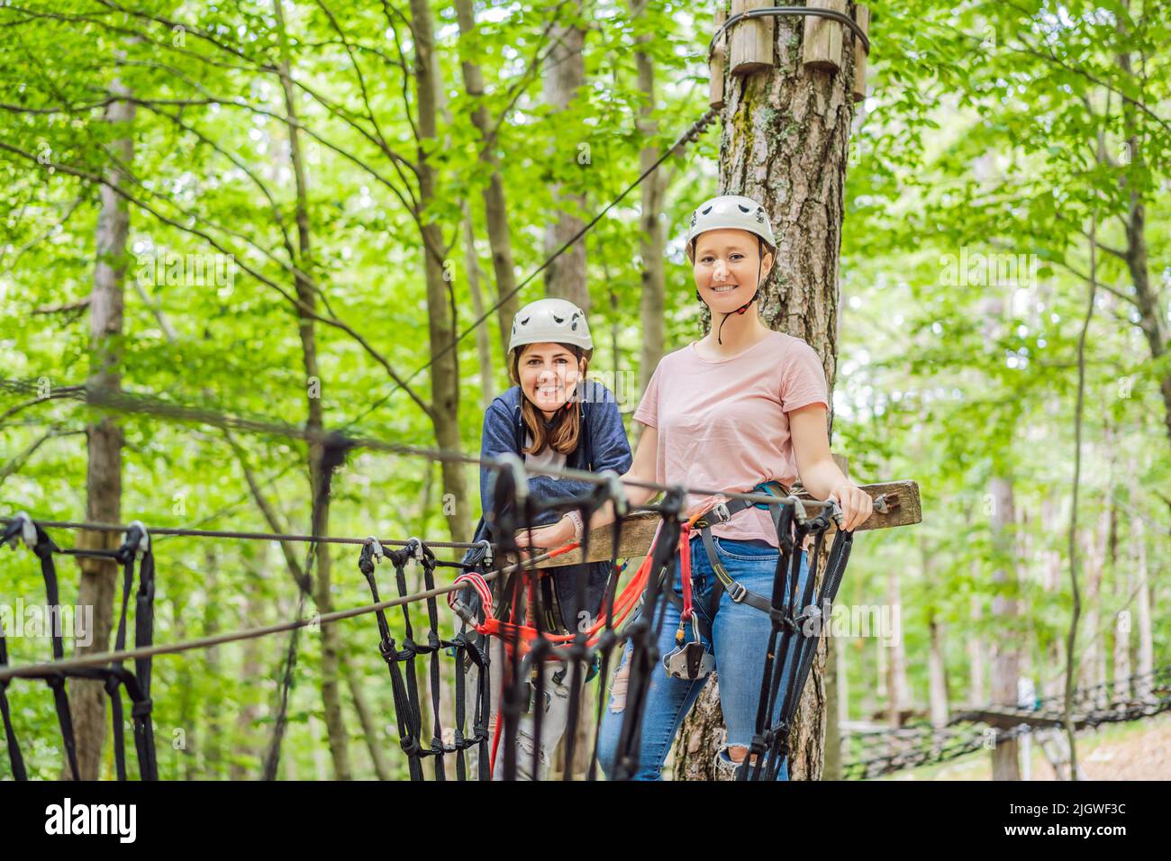Two women girls female gliding climbing in extreme road trolley zipline in forest on carabiner