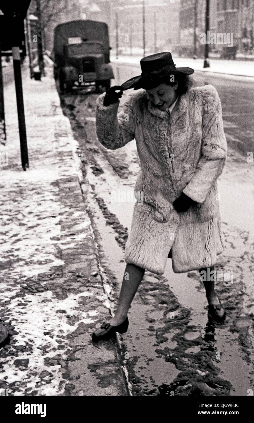 Szene aus dem Nachkriegs-Berlin - Junge Frau in einem Pelzmantel schleicht in Sommerschuhen durch den Schneematsch in Berlin, Deutschland 1947. Stock Photo