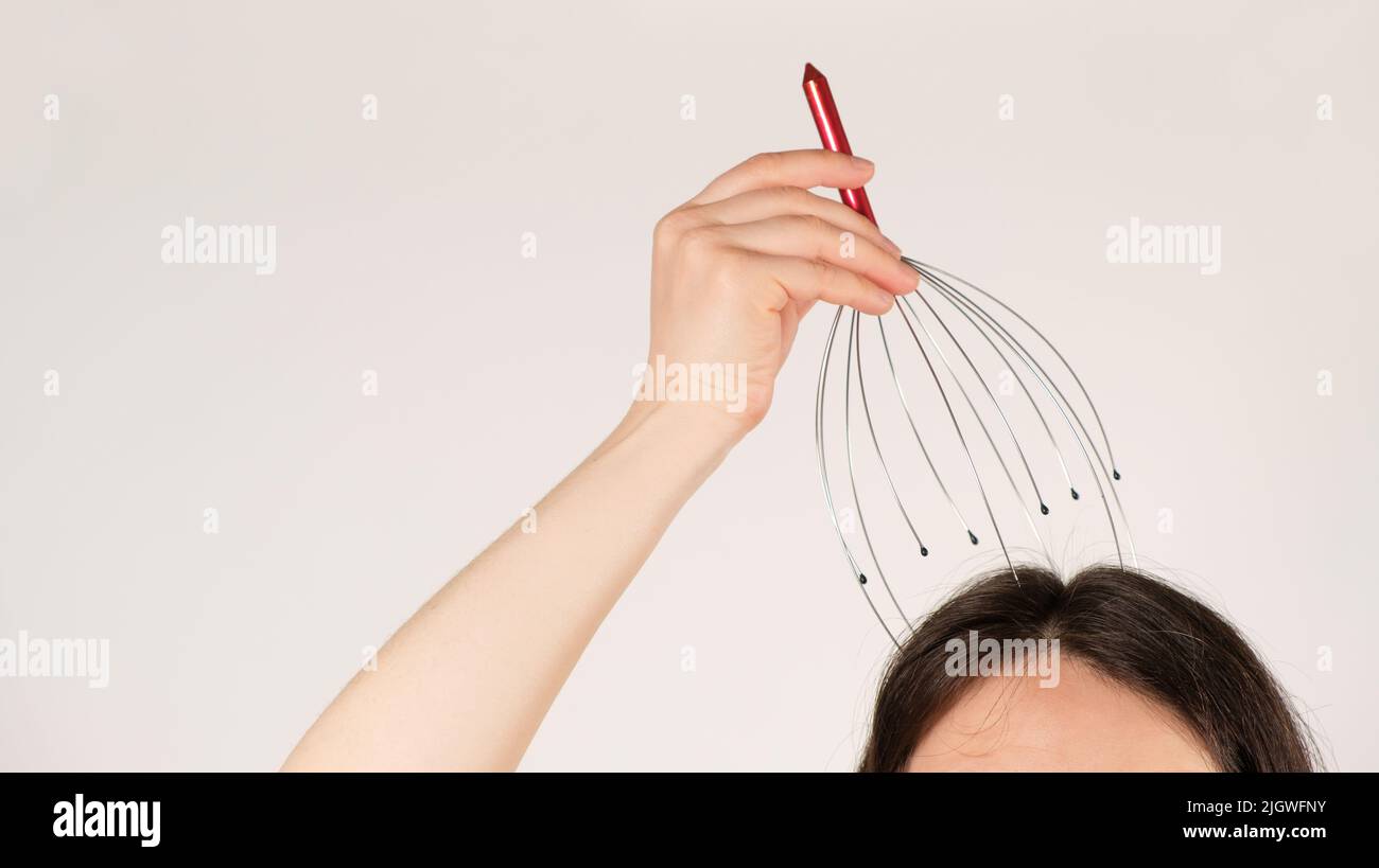 A woman with a metal flexible massager for self-massage of the head on a white background, copy the place for the text Stock Photo