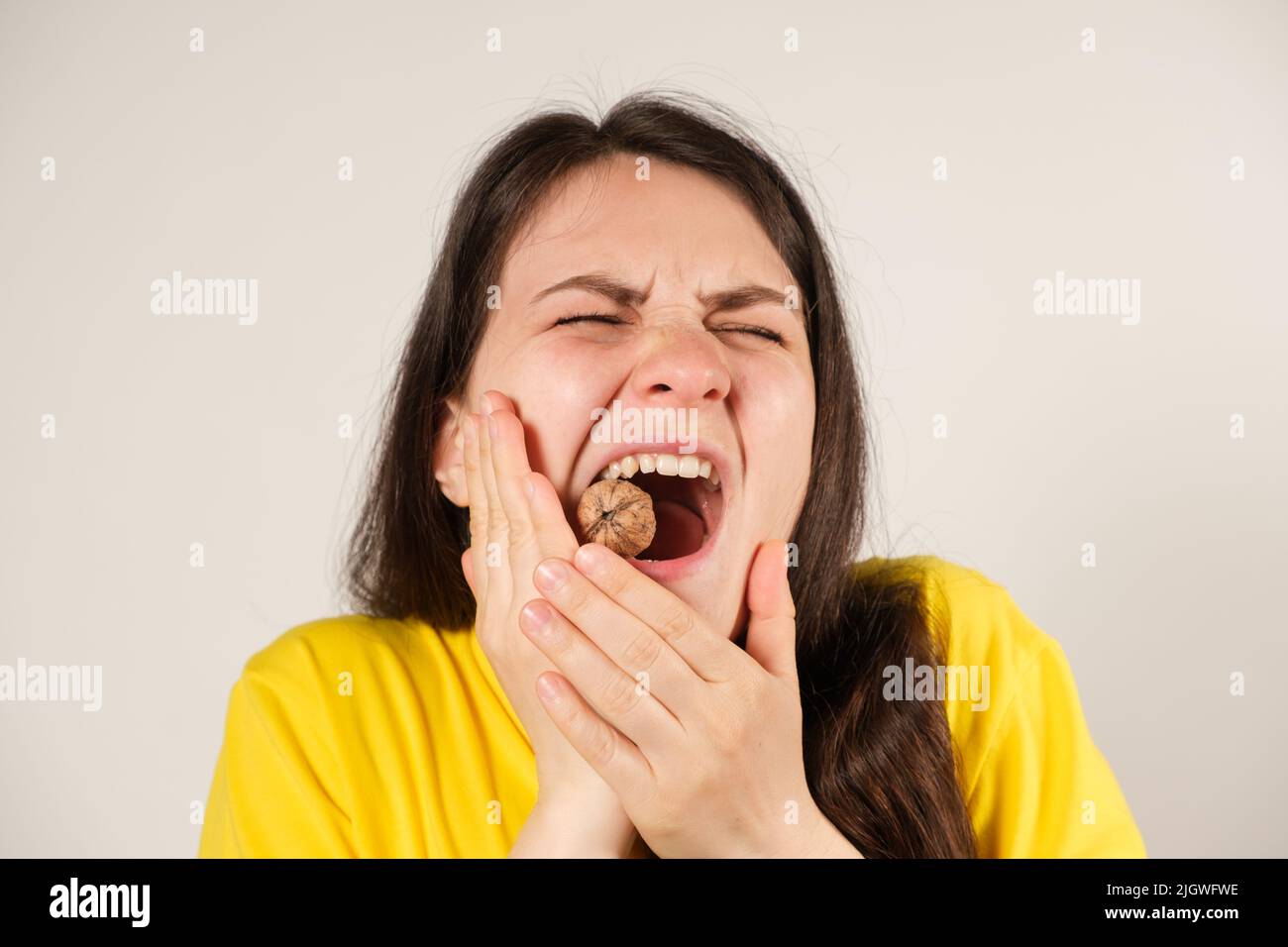 A woman gnaws on a walnut, opening her mouth wide, breaking a tooth or dislocating the temporomandibular joint, her jaw has moved away. Stock Photo