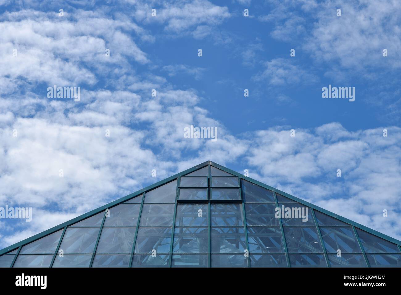 Abstract view of a modern buildings pointed roof leading to a blue sky with fluffy clouds. Stock Photo