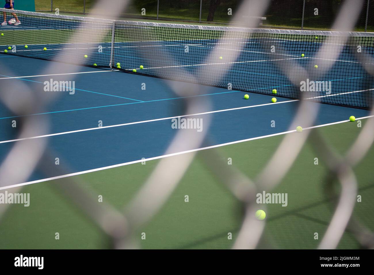 looking through a Galvanized Chain Link fence at a tennis court with light green balls Stock Photo