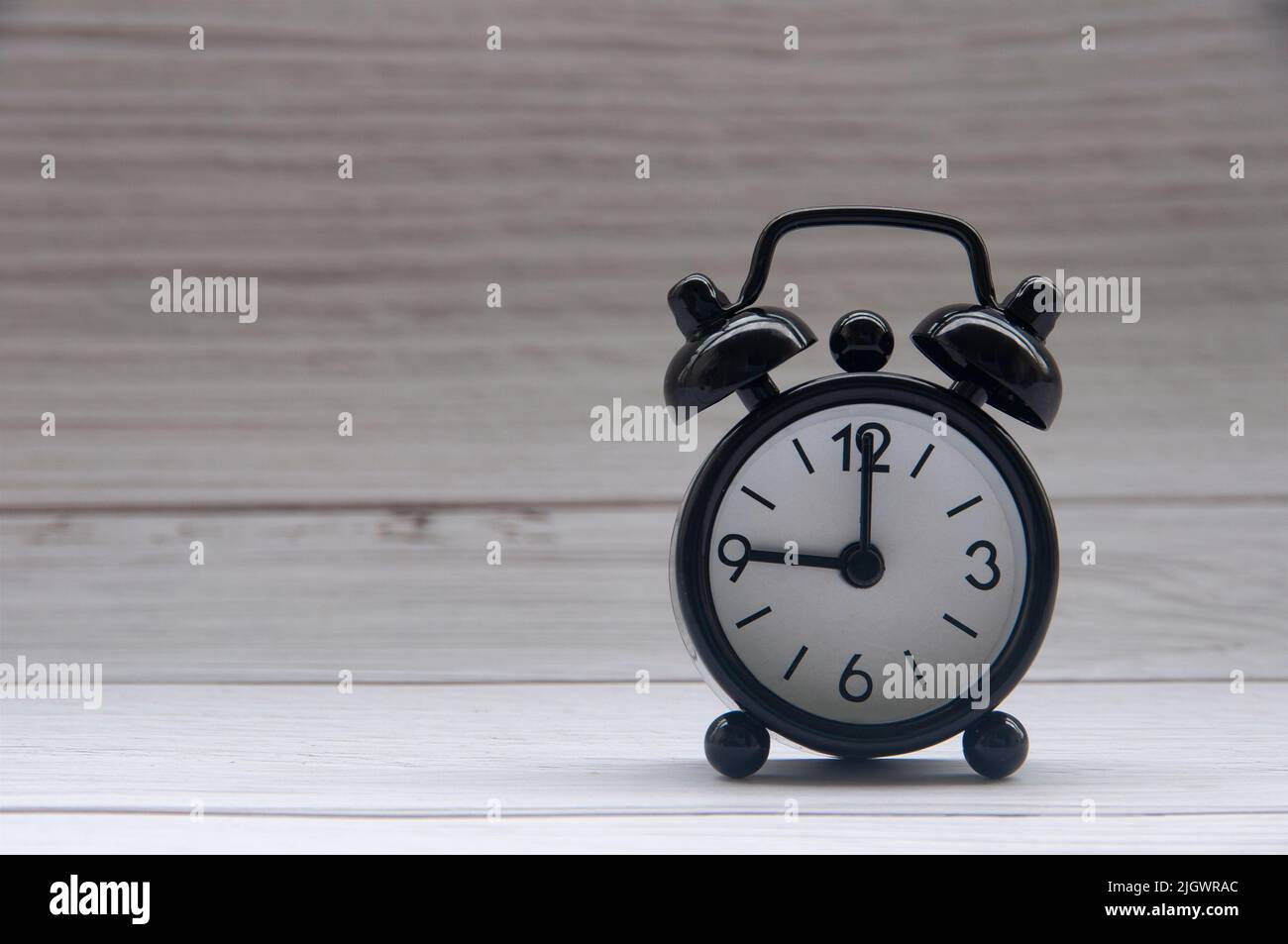 Black alarm clock isolated on wooden cover background. The clock set at 9 o'clock. Copy space. Stock Photo