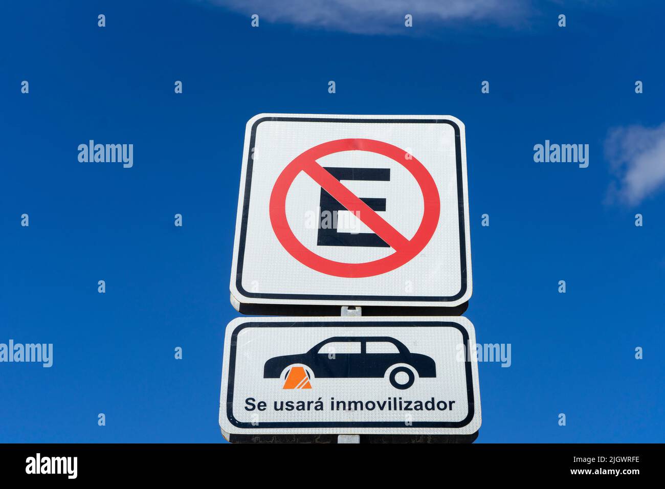 Parking ban sign with Spanish-language wheel block, against blue sky Stock Photo