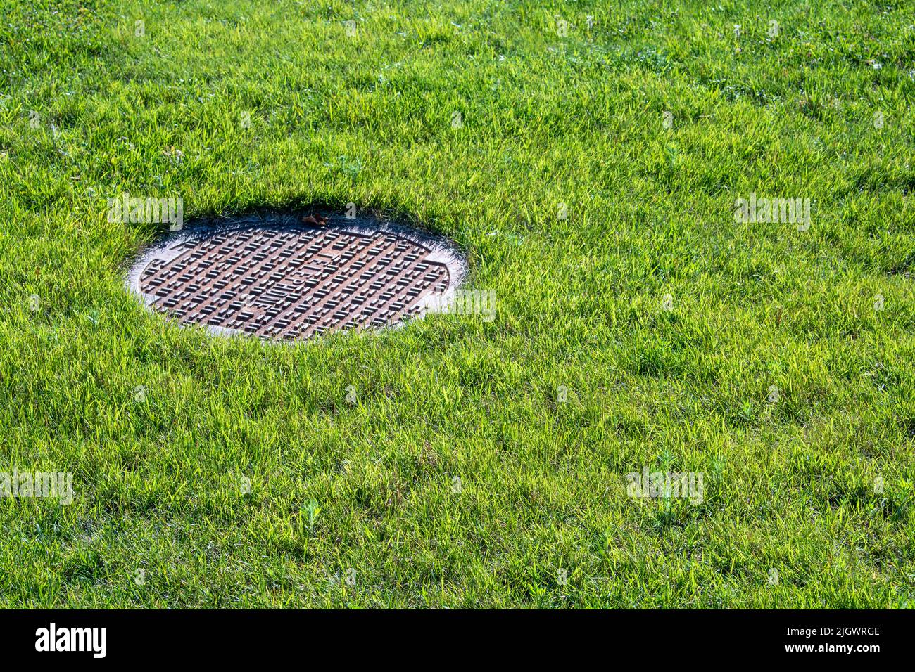 Grass and cast iron Manhole Cover Stock Photo