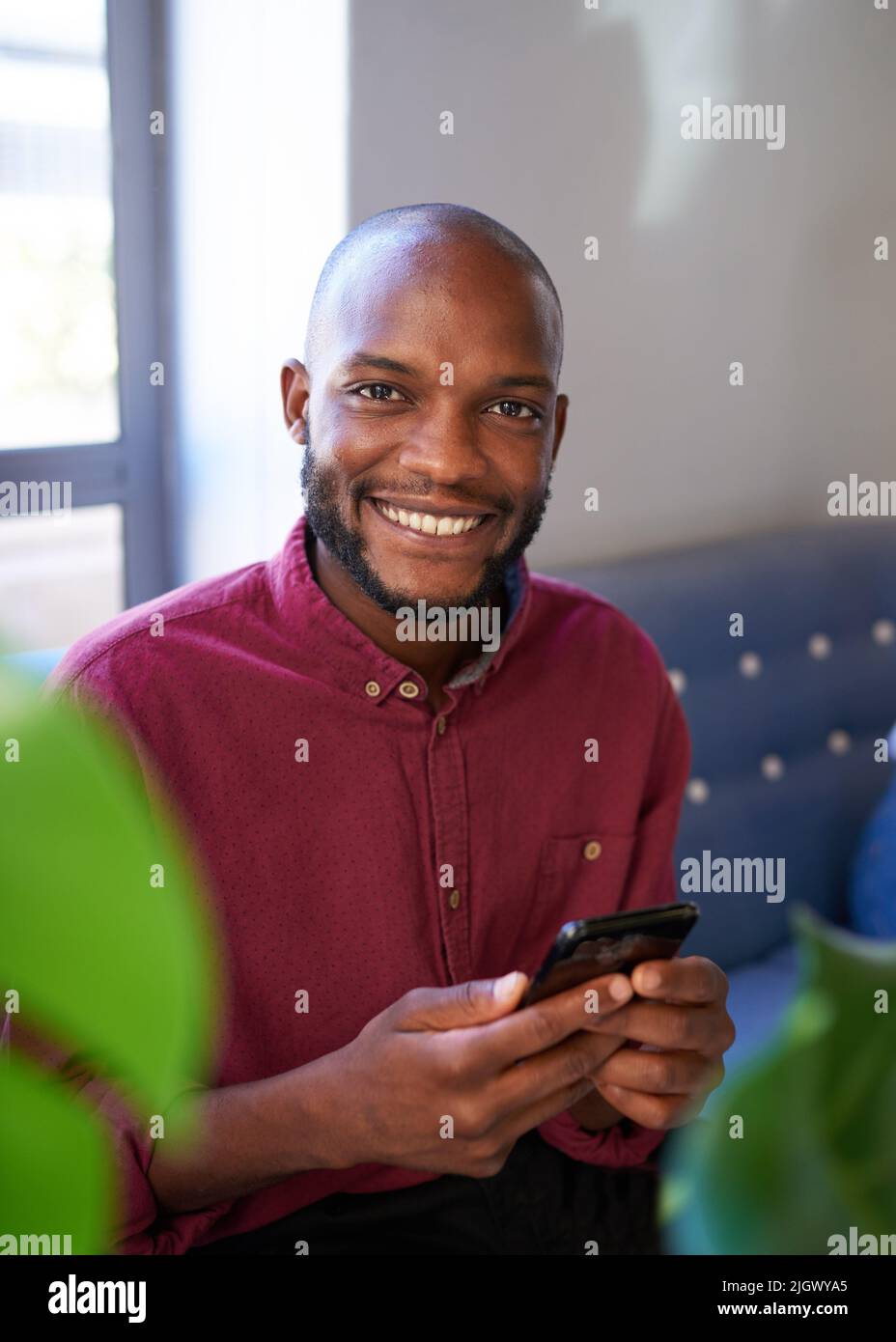 An attractive Black man smiles at the camera while using his phone Stock Photo