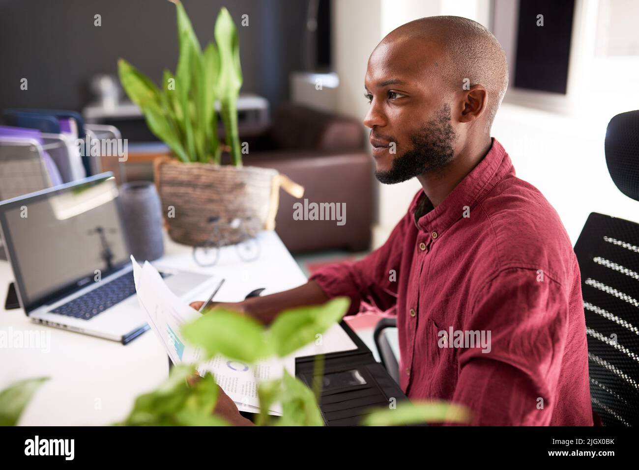 A Black man sits at his office desk with notes and laptop Stock Photo