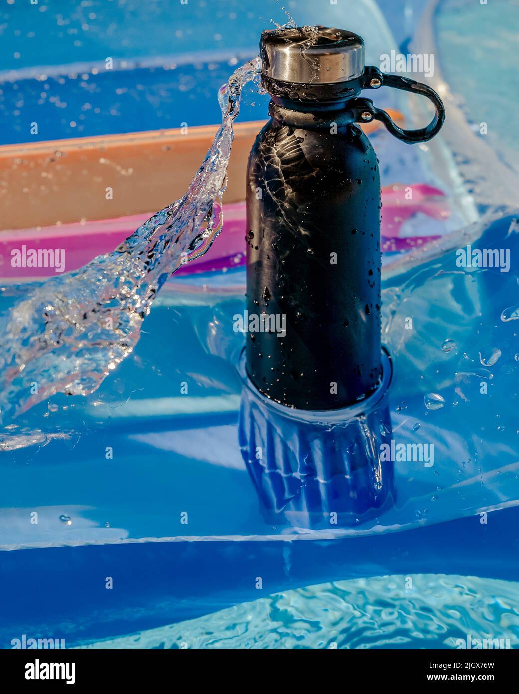 A black insulated bottle on an air mattress with a spray of water hitting it Stock Photo