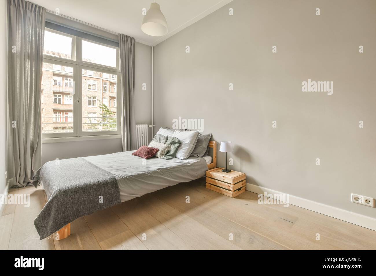 Comfortable bed with colorful pillows and warm blanket located near window in stylish bedroom