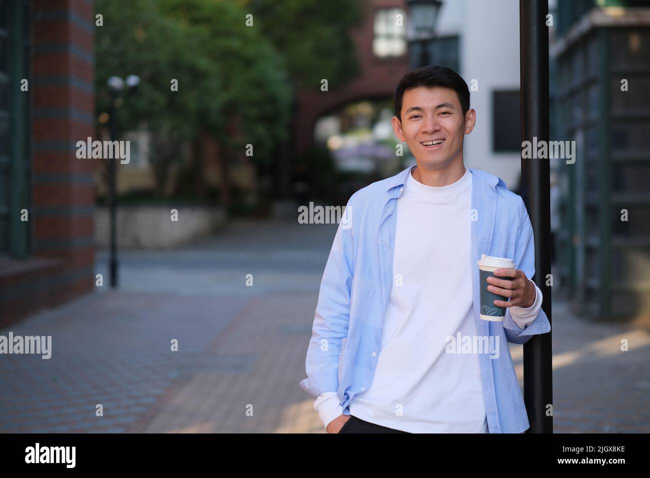smiling Asian young man holding a cup of coffee on the street, looking at camera Stock Photo