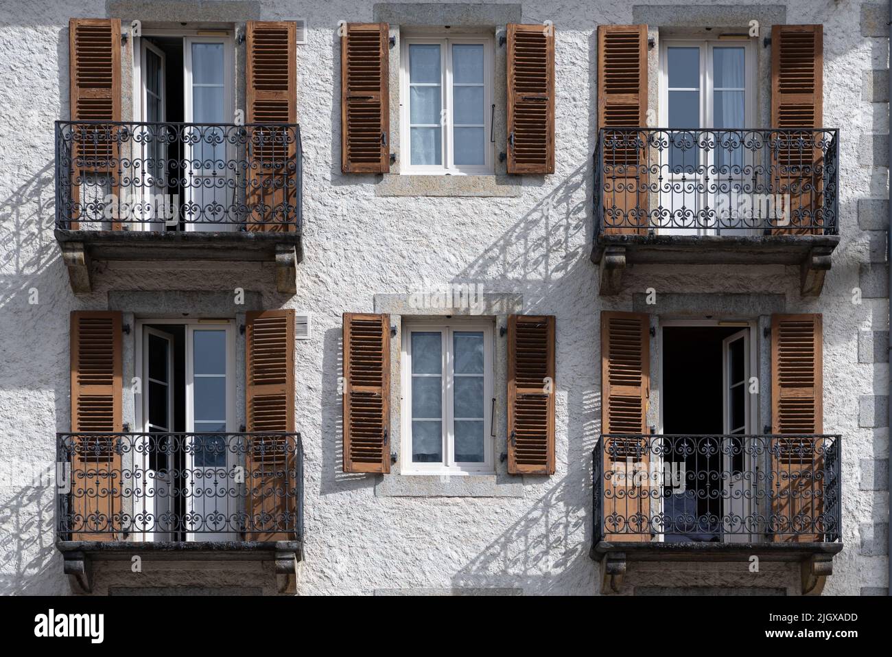 Wrought iron balcony railings with wood shutter doors and windows in rendered wall exterior facade in afternoon sunlight casting shadows on wall in Ch Stock Photo