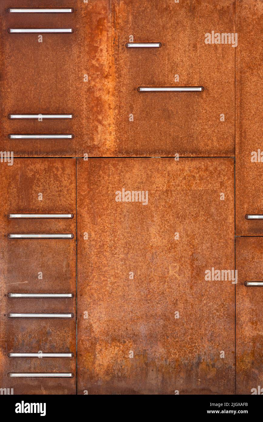 Square rusty red steel plates in various dimensions cladding facade walls of contemporary modern architecture building with various design features in Stock Photo